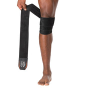 HyperWrap Multi-Use Compression Wrap by Shock Doctor shown in black, providing adjustable support for wrist and knee with wrap-around design. Model wrapping it around their patella.