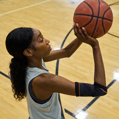 Female Basketball Athlete Shooting Ball While Wearing Shock Doctor Compression Knit Elbow Sleeve with Gel Support